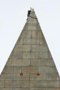 Horolezec pripevňuje laná na vrchol obelisku. Červené body sú signálne svetlá pre lietadlá.