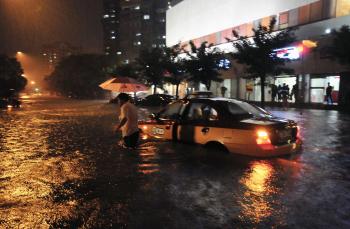 Taxikár opúšťa svoje auto, ktoré uviazlo v zaplavenej ulici