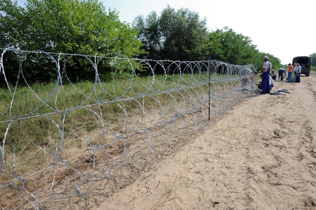 Na snímke maďarskí pracovníci upevňujú žiletkový ostnaný drôt na konštrukciu plotu na maďarsko-srbských hraniciach neďaleko maďarského mesta Morahalom