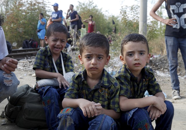 Na snímke traja malí migranti oddychujú vedľa svojich rodičov po príchode do  mesta Gevgelija na juhu Macedónska