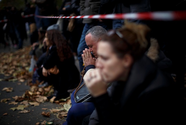 Žena a muž sa modlia pred kvetmi a sviečkami pri divadle Bataclan na znak úcty k mŕtvym, ktorí prišli o život počas piatkového teroristického útoku v Paríži