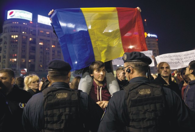 Demonštrant drží rumunskú zástavu počas protestu pred vládnymi sídlami na Námestí Víťazstva v Bukurešti