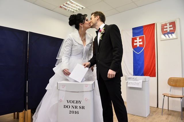 Ženích Ondrej Šulc (vpravo) a nevesta Petra Schönová sa bozkávajú pri vhadzovaní obálok s hlasovacími lístkami do volebnej schránky vo voľbách do Národnej rady SR vo volebnej miestnosti v Dubnici nad Váhom 5. marca 2016