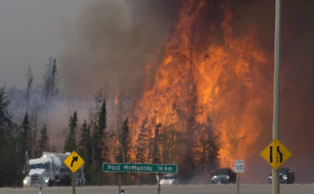 Na archívnej snímke z 6. mája 2016 autá prechádzajú neďaleko obrovských plameňov 16 km južne od Fort McMurray