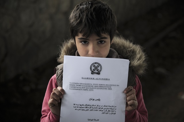 Migrantský chlapec drží dokument, ktorý migrantom rozdáva grécka polícia v utečeneckom tábore