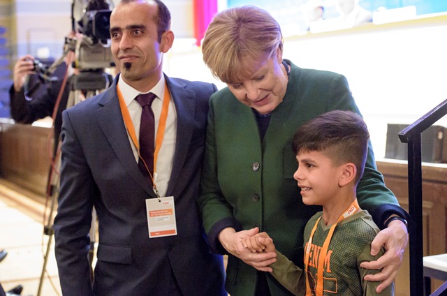 Na snímke nemecká kancelárka Angela Merkelová (uprostred) a malý Afganec Edris sa držia za ruku na zjazde Merkelovej Kresťanskodemokratickej únie (CDU)
